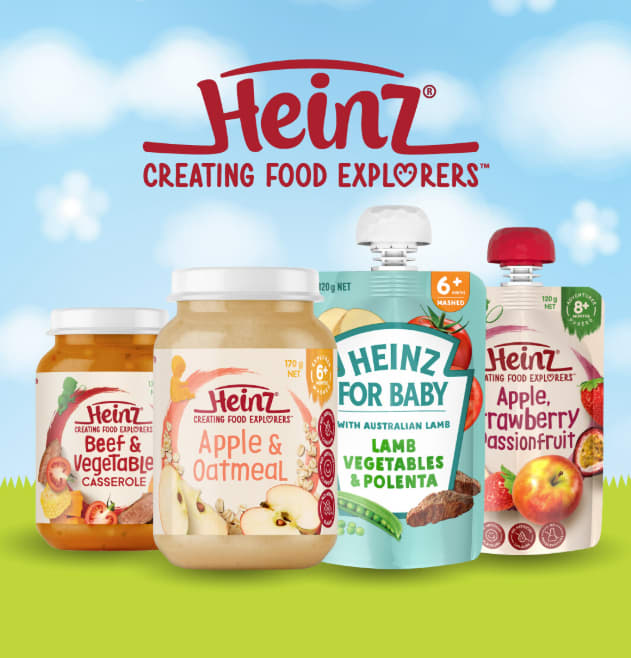 An assortment of Heinz baby food products displayed against a cheerful backdrop of blue skies and a green field.
