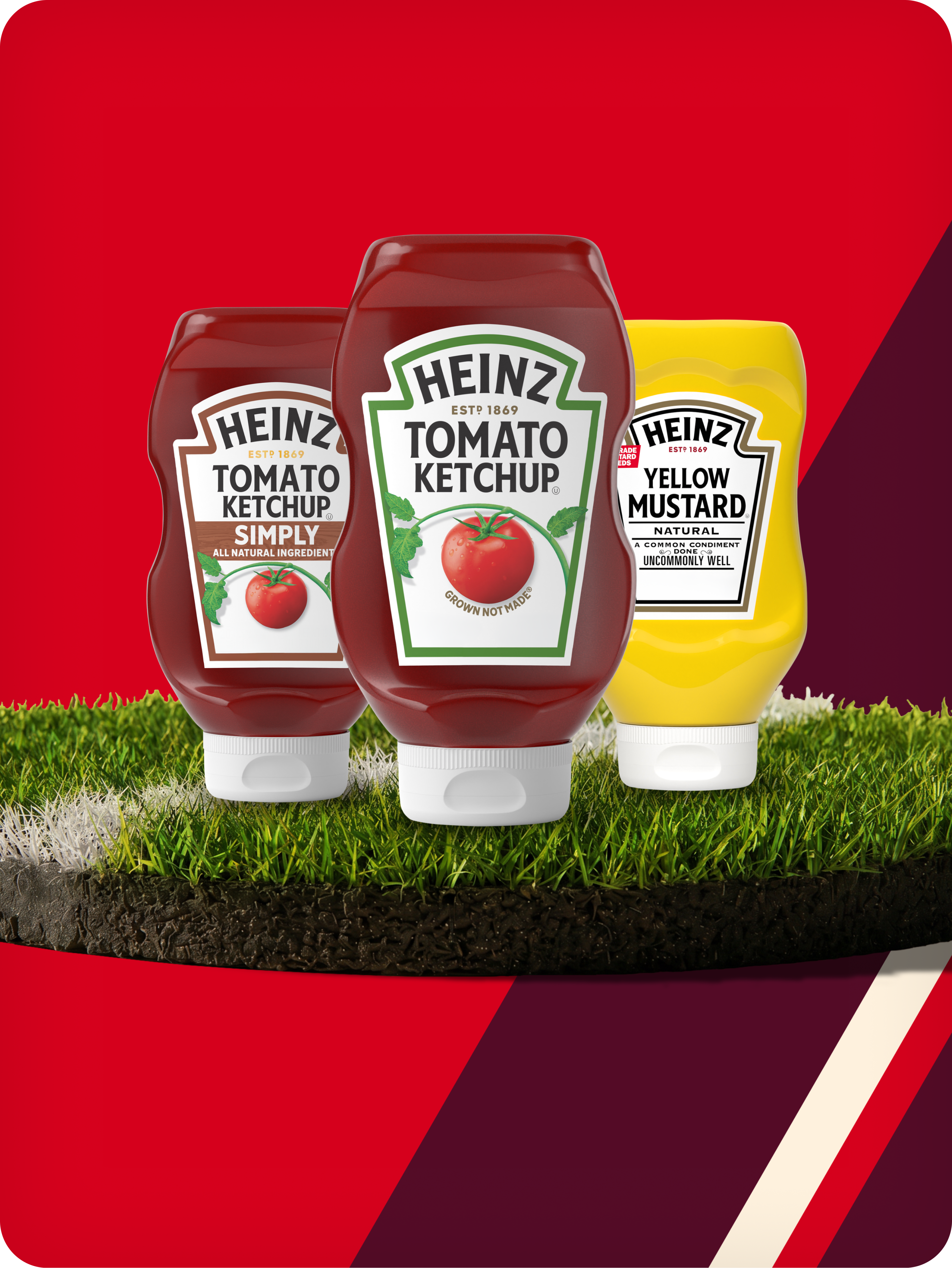 Three squeeze bottles of Heinz Ketchup and Yellow Mustard standing on a patch of stadium grass.