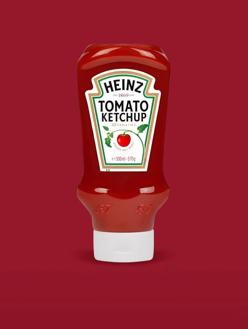 A squeeze bottle of Heinz Tomato Ketchup with a red tomato on its label, against a dark red background.