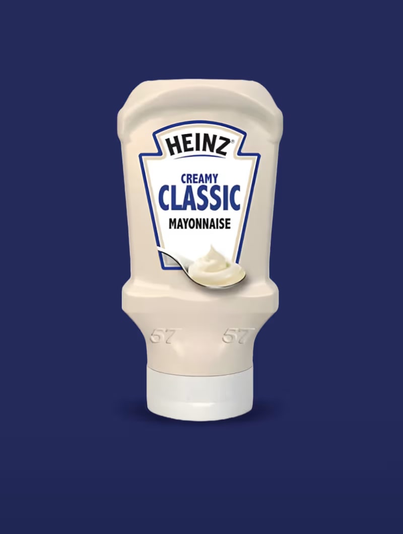 A white squeeze bottle of Heinz Creamy Classic Mayonnaise, against a dark blue background.