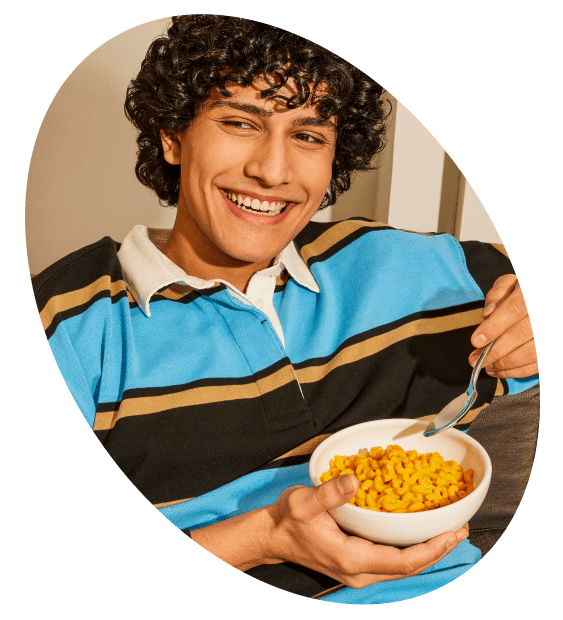 Young man smiles and eats macaroni and cheese.