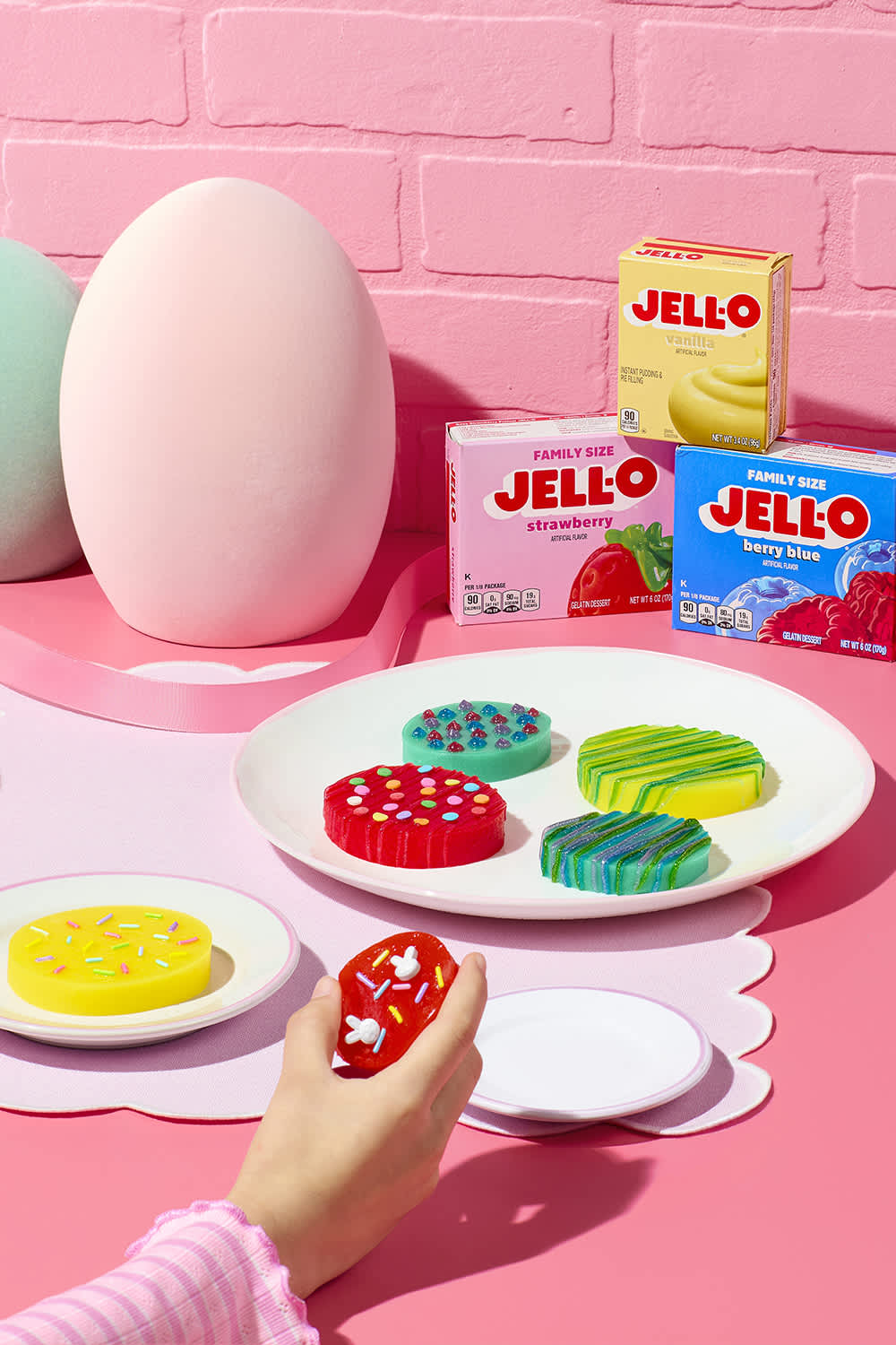 Brightly colored Jell-O Jigglers decorated with sprinkles on a pink table with a large white Easter egg.