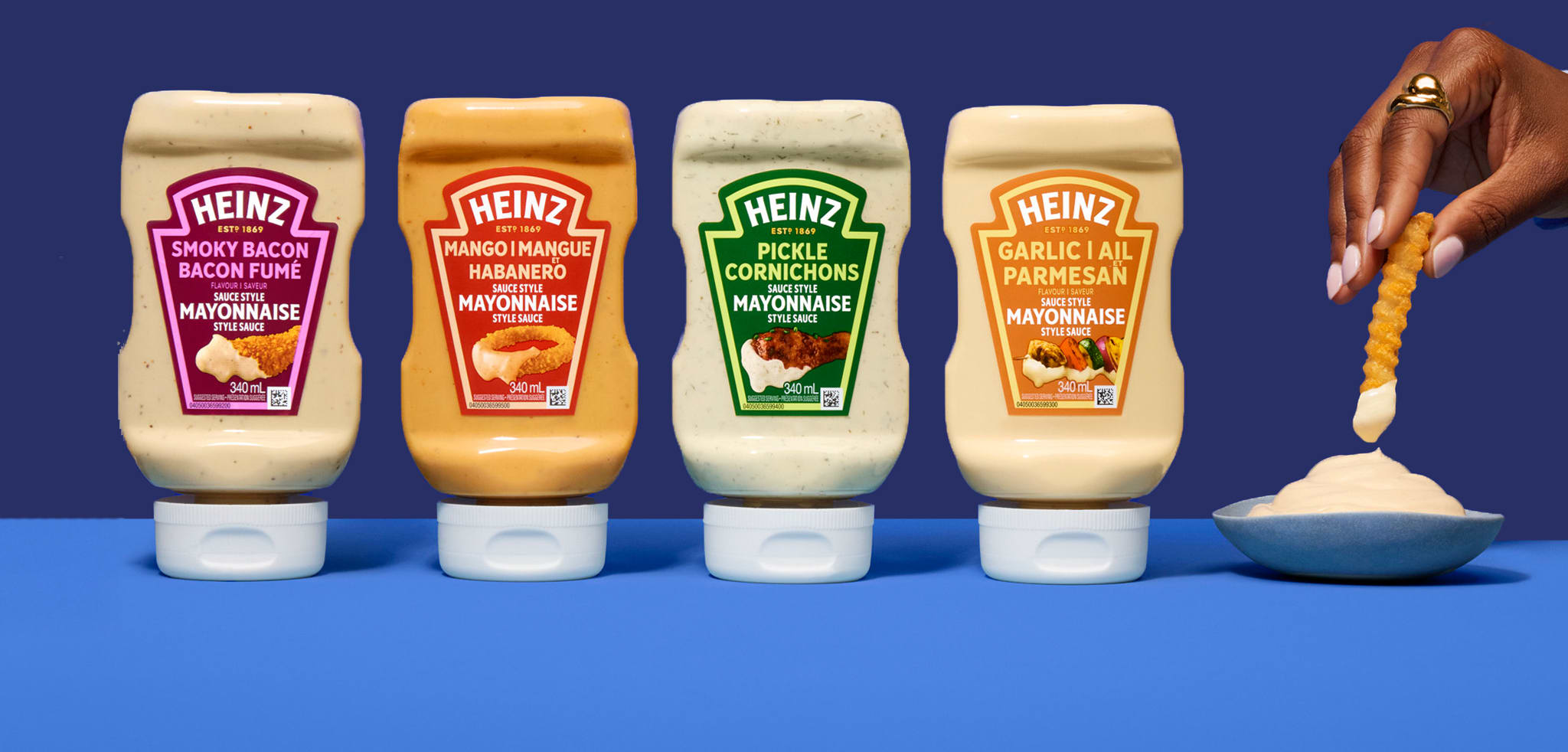 Quatre bouteilles de sauces style mayonnaise Heinz, incluant Bacon Fumé, Mangue Habanero, Cornichons Marinés et Ail Parmesan.