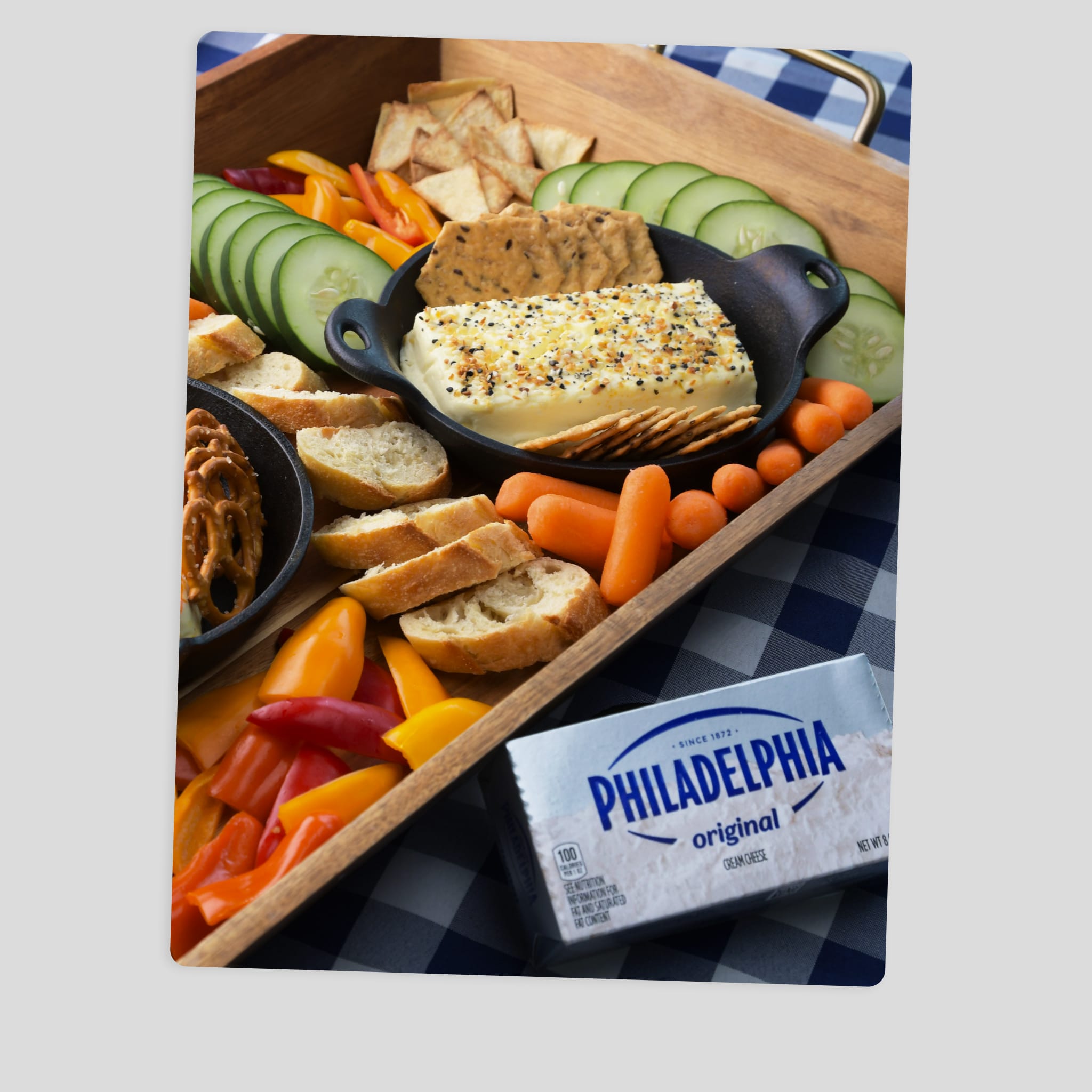 An assortment of snack items arranged on a wooden tray, including sliced baguette, cucumber slices, among other vegetables. 