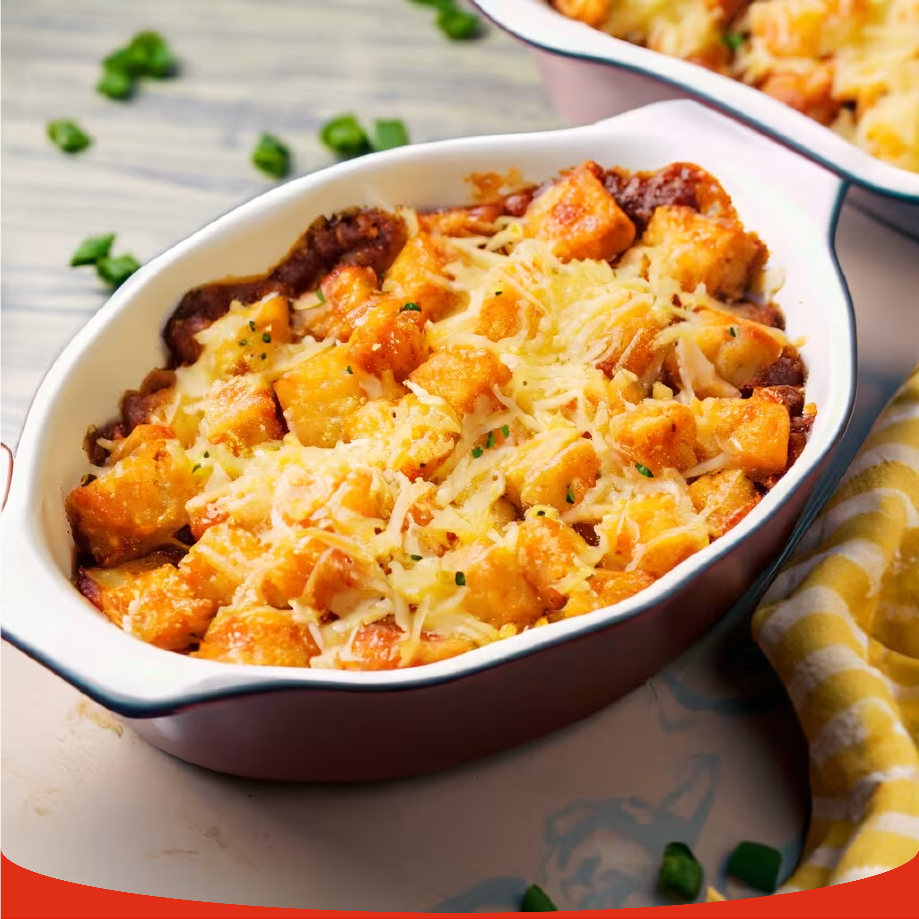 A close-up of a bubbling cheesy baked potato casserole in a white and brown oval dish, garnished with fresh chives.