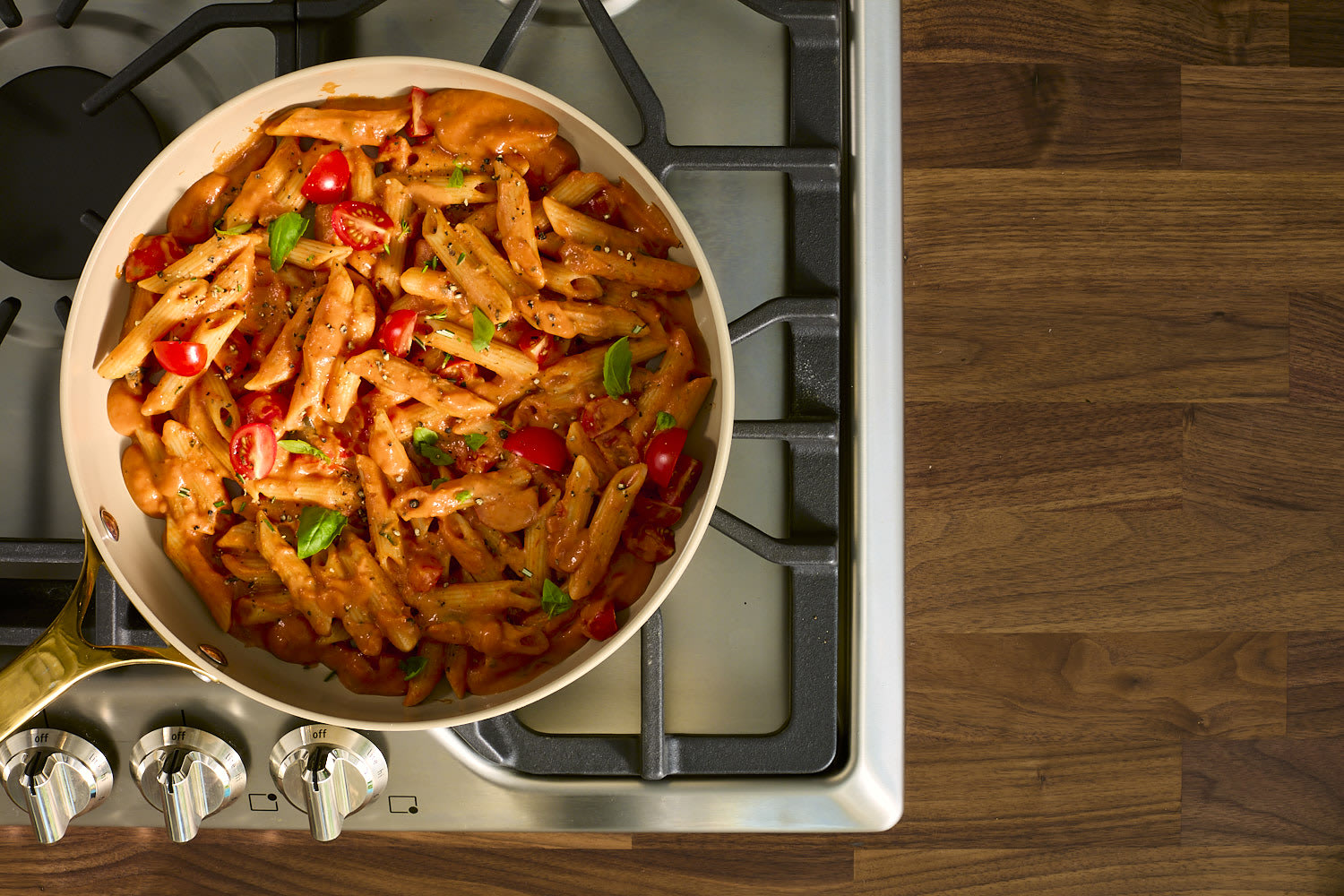 A skillet of creamy tomato penne pasta, garnished with fresh basil, sits on a stovetop.
