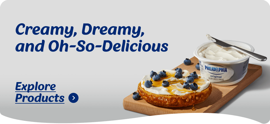 Philadelphia Original Cream Cheese spread generously on a bagel, topped with fresh blueberries and a golden honey drizzle