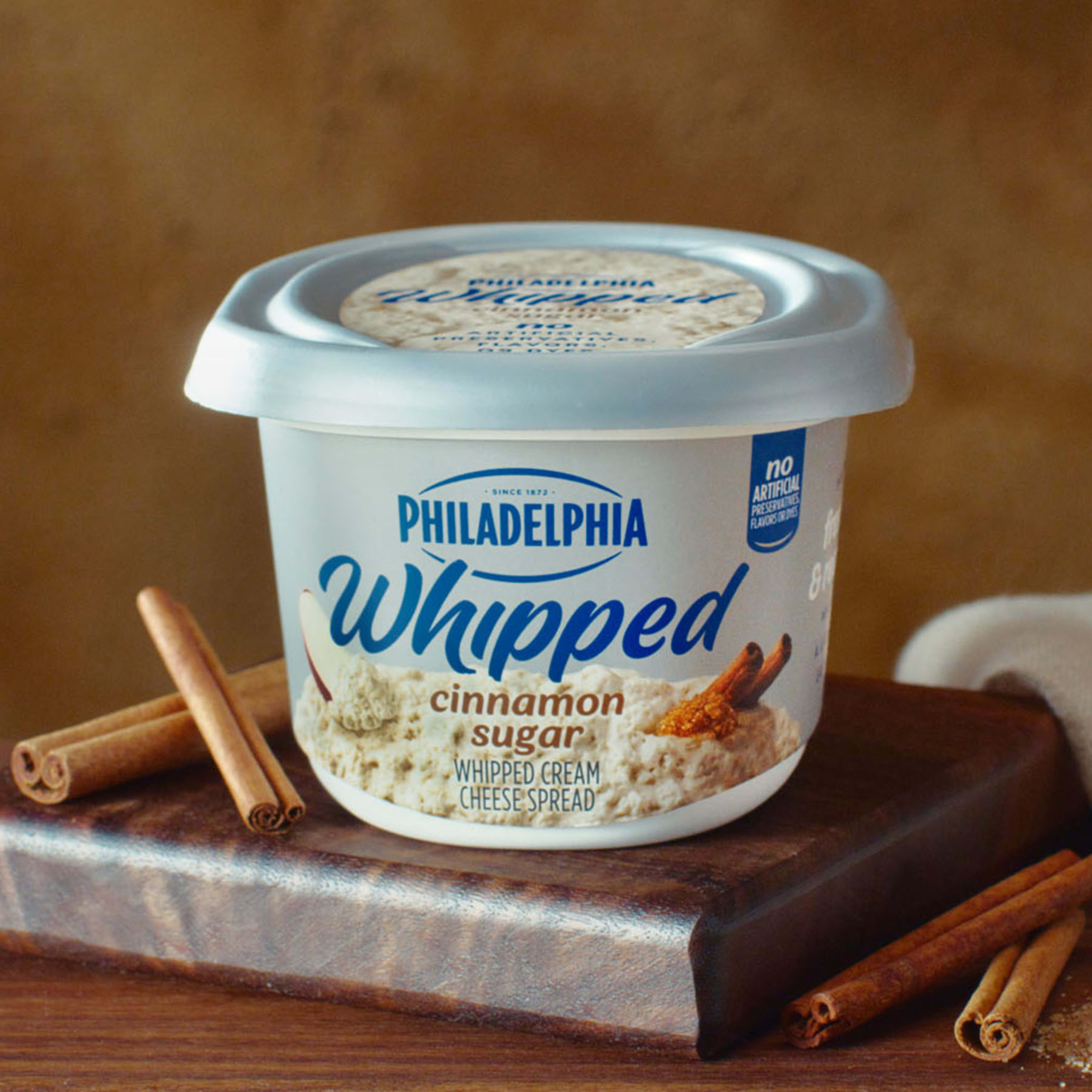A tub of Philadelphia Whipped Cinnamon Sugar cream cheese surrounded by cinnamon sticks.