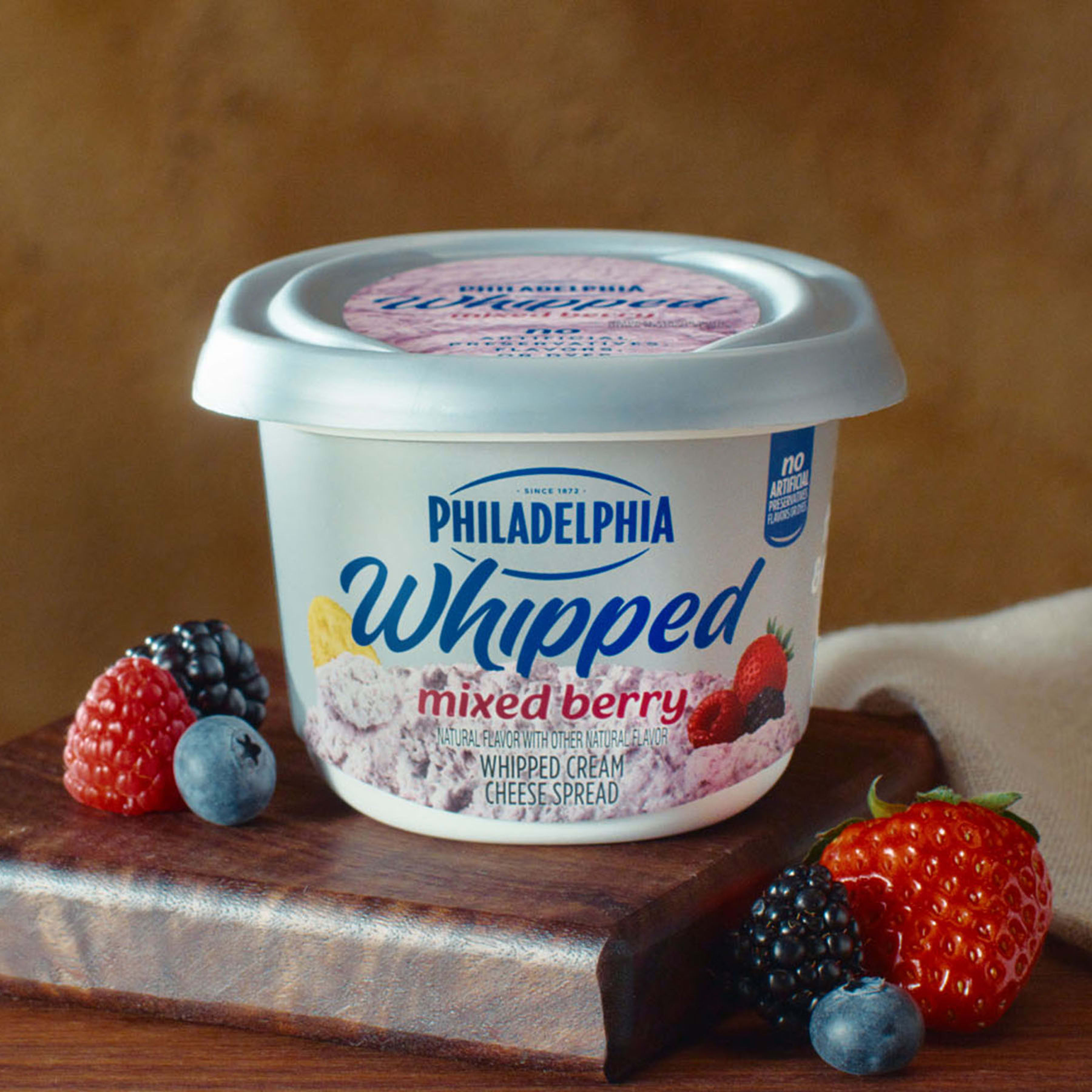A tub of Philadelphia Whipped Mixed Berry cream cheese surrounded by fresh berries.