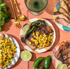 An overhead shot of a table spread with grilled food, including steak, corn salad, and jalapenos.