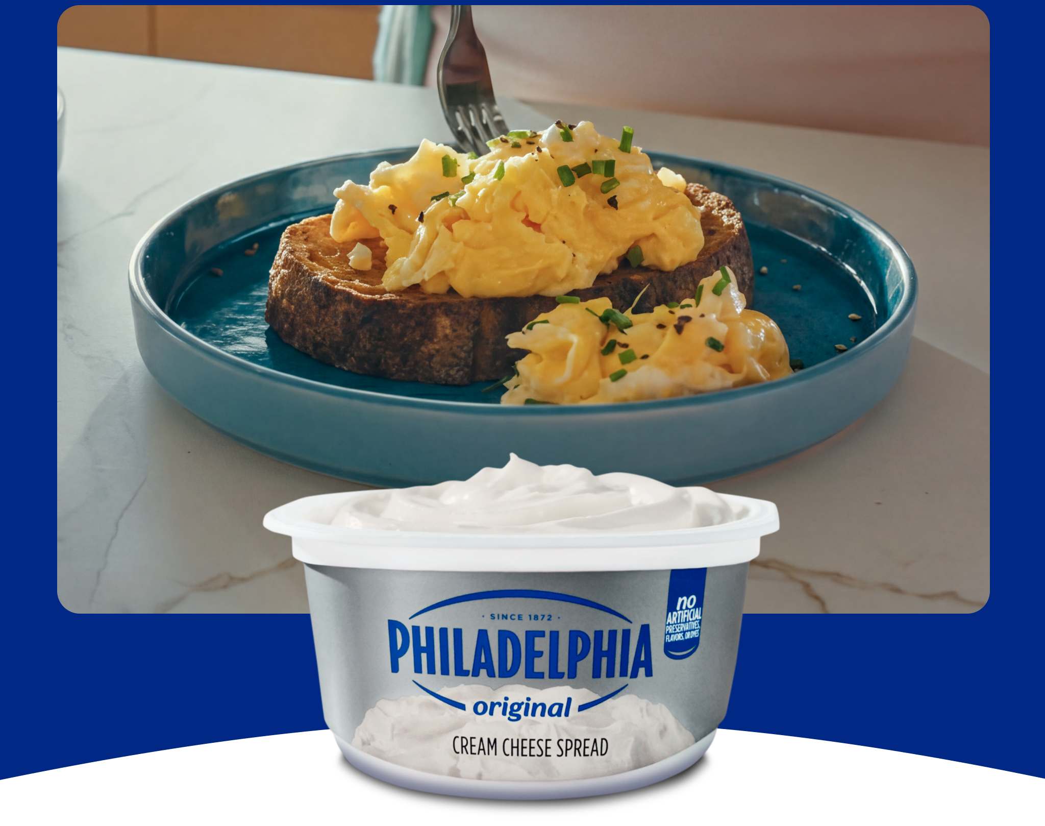 A photo of a dish with a toast with creamy scrambled eggs and a tub of Philadelphia Cream Cheese