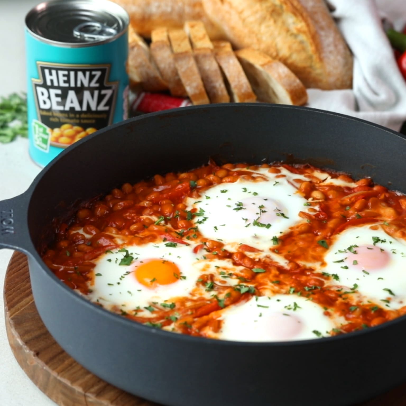 Heinz Beanz baked eggs recipe: A skillet filled with Heinz Beanz in tomato sauce, topped with baked eggs and parsley.