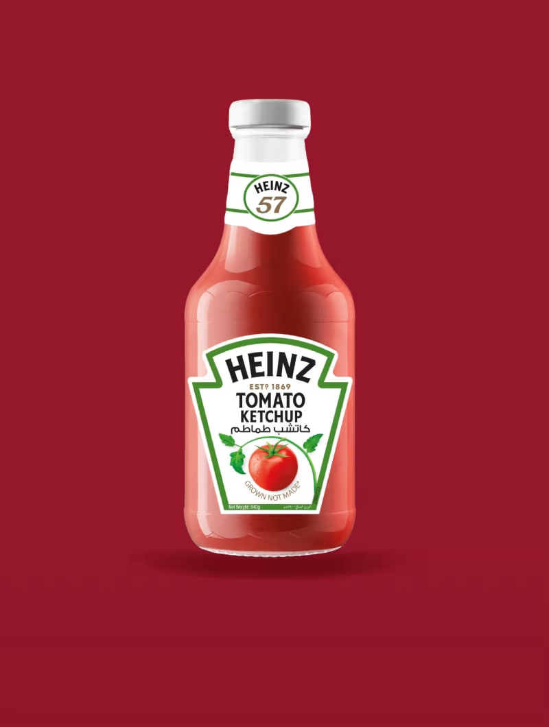 زجاجة كاتشب هاينز مع ملصق أخضر وطماطم حمراء على خلفية حمراء داكنة.