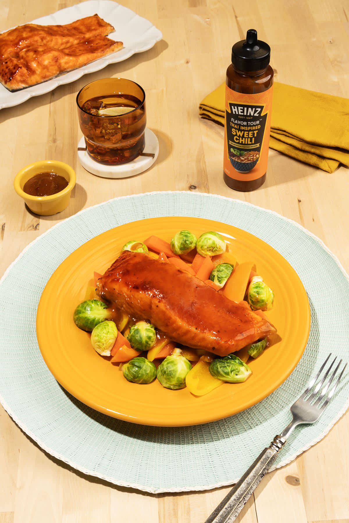 Flaky salmon fillet glazed with Heinz Thai Inspired Sweet Chili Sauce, served on a vibrant orange plate with a side of roaste
