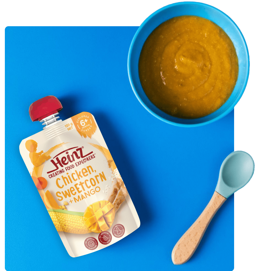 Heinz chicken, corn and mango baby food in pouch next to bowl and spoon.