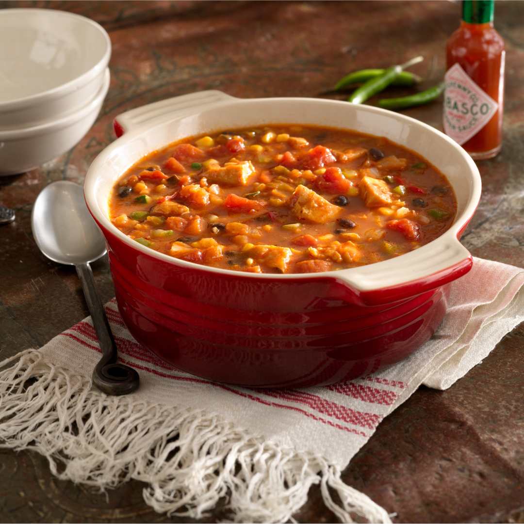 Bowl of chicken soup with vegetables and a bottle of Tabasco.