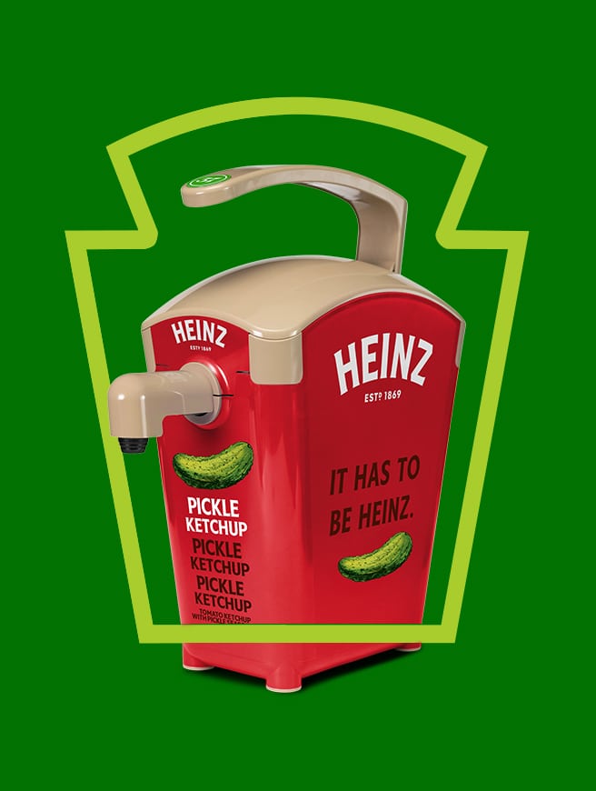  A red Heinz Pickle Ketchup dispenser with a tan pump, framed by a lime green keystone outline on a dark green background.