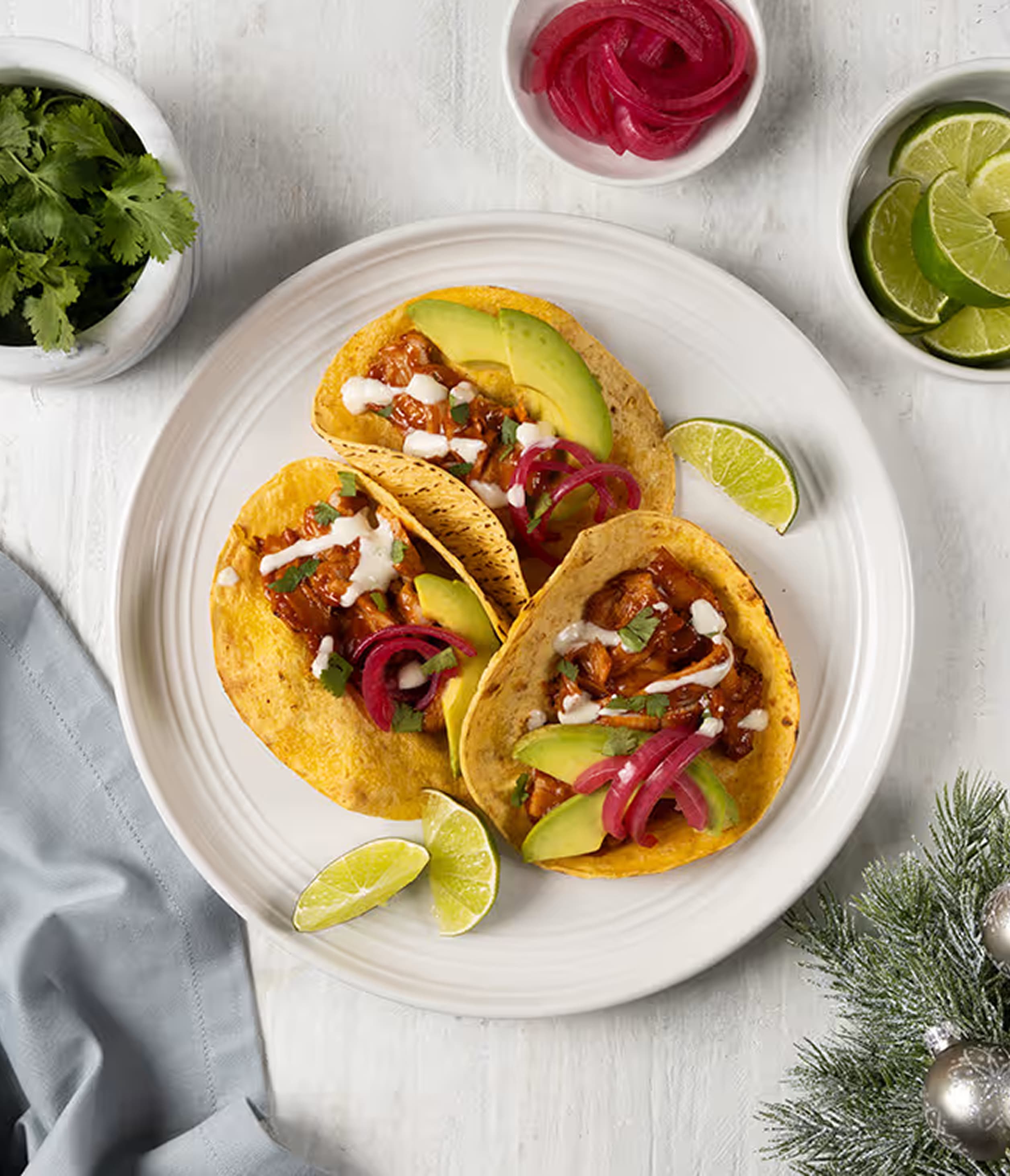 Three turkey tinga tacos are beautifully arranged on a white plate. The golden-yellow corn tortillas are filled with a vibran