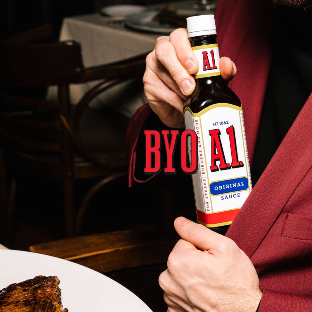 A person holding a bottle of A1 sauce next to a steak and potato dish.