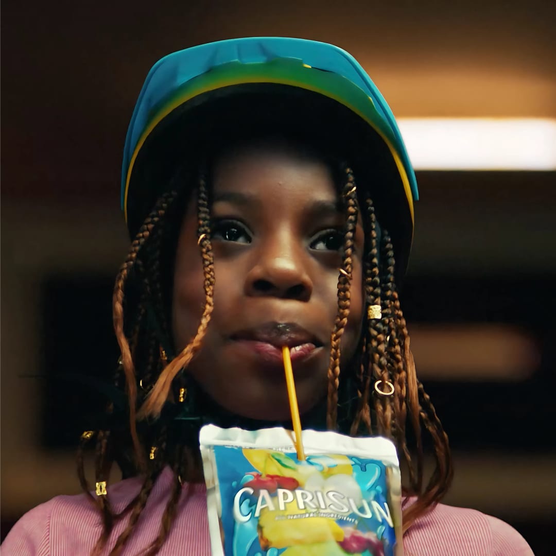 Girl with braids drinks Capri-Sun with a blue head covering.