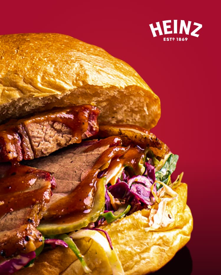 A roast beef sandwich on a crusty roll topped with pickles, cabbage, and BBQ Sauce.