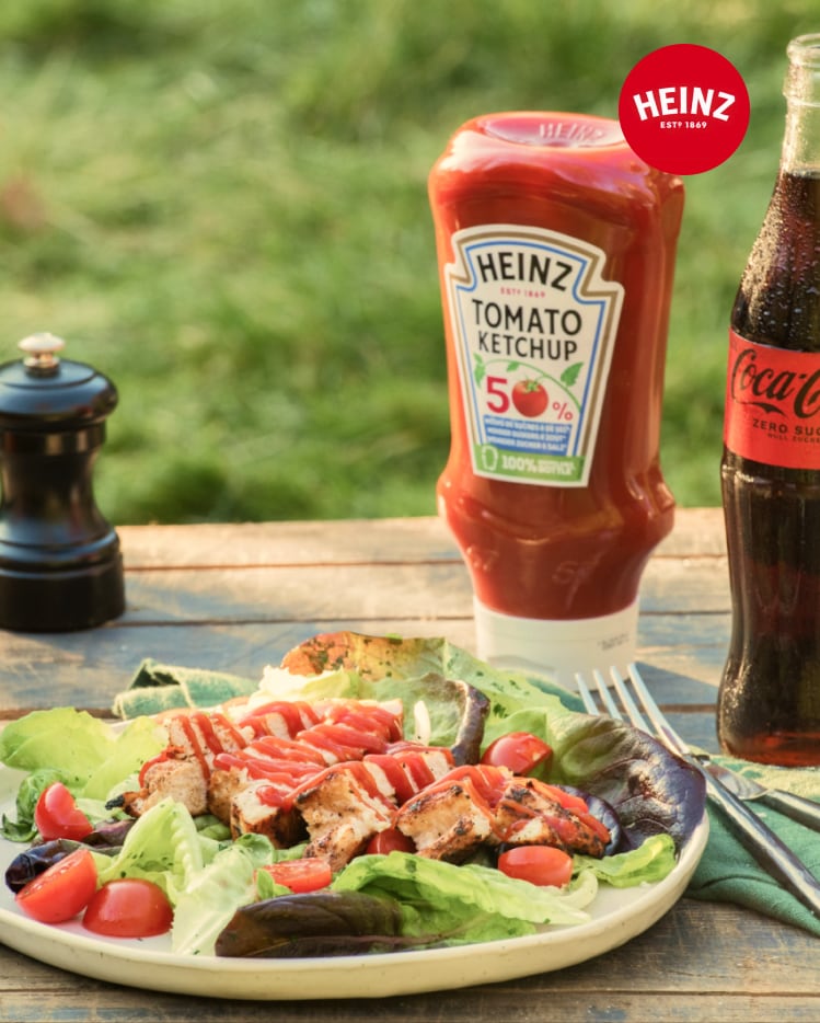 Grilled chicken salad with Heinz ketchup, a Coca-Cola, and a pepper grinder outdoors.