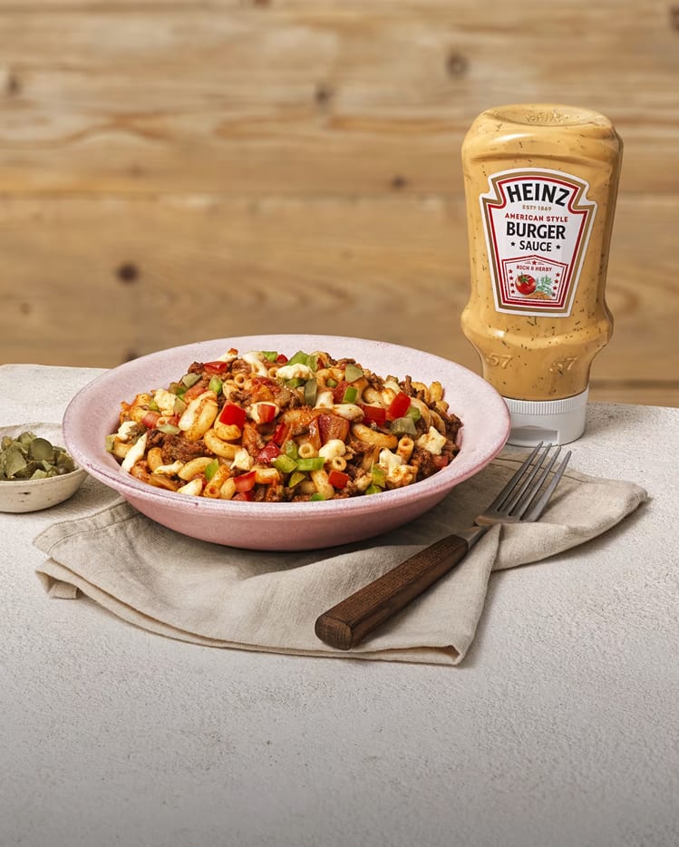 A bowl of macaroni pasta mixed with ground beef, tomatoes, and greens, served with Heinz American Style Burger Sauce.