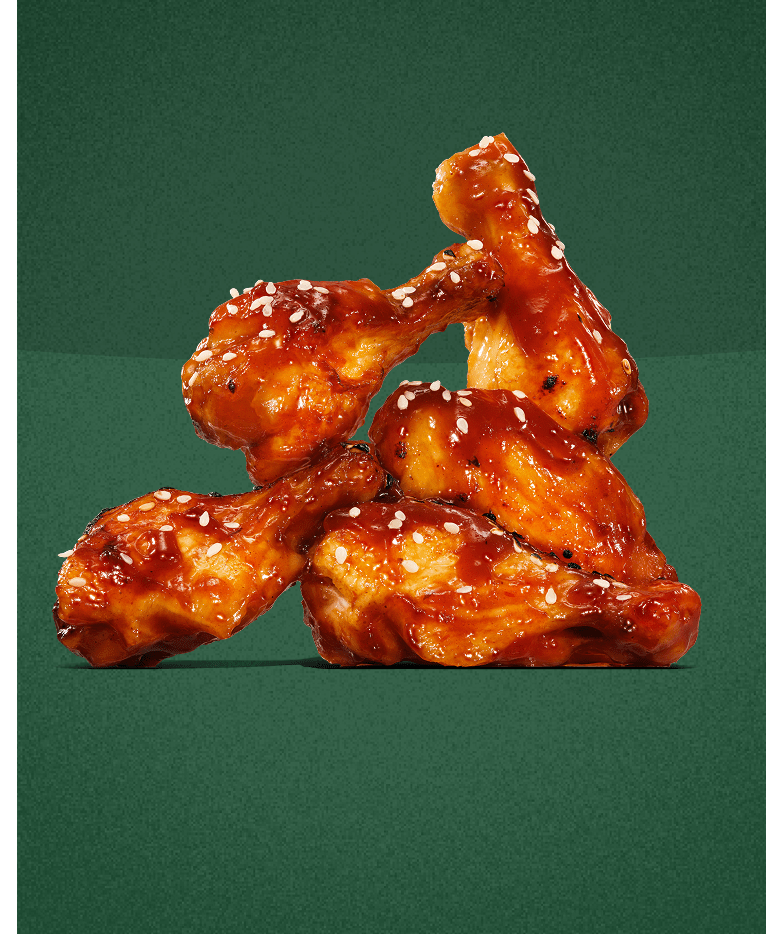 A stack of glazed chicken wings topped with sesame seeds against a dark green background.