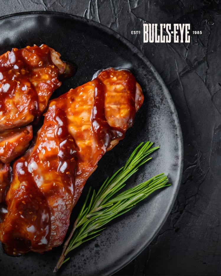 BBQ glazed ribs on a black plate with rosemary and a Bull's-Eye logo.