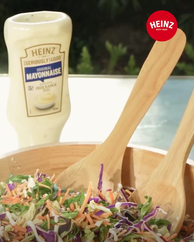 A large wooden bowl of coleslaw with a bottle of Heinz Mayonnaise.