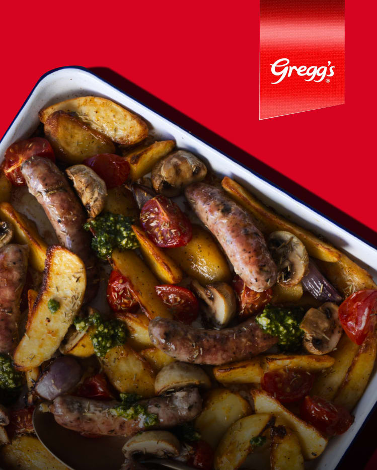 Tray bake of sausages, potatoes, tomatoes, and pesto.
