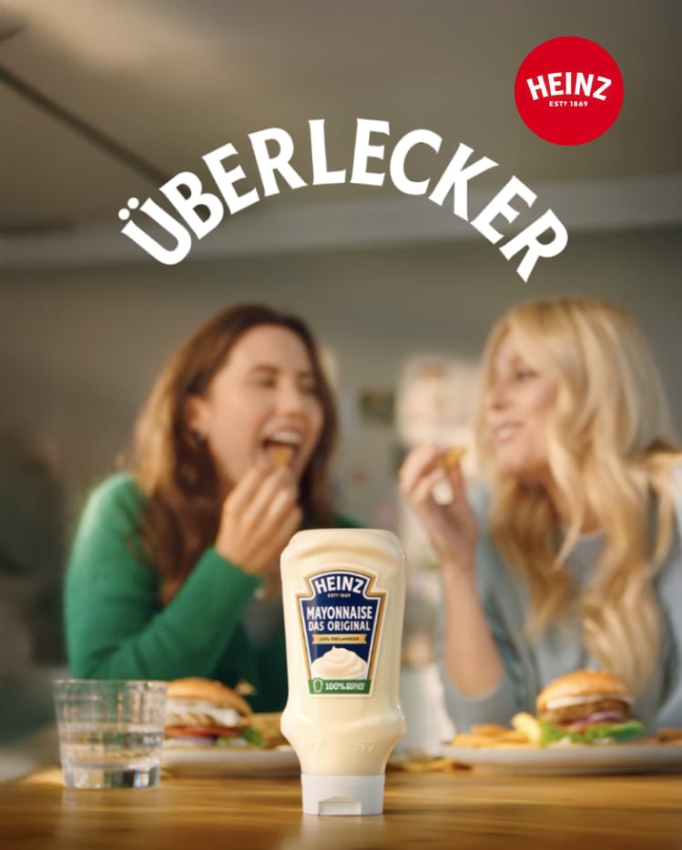 A bottle of Heinz Mayonnaise with two women blurred in the background eating burgers.
