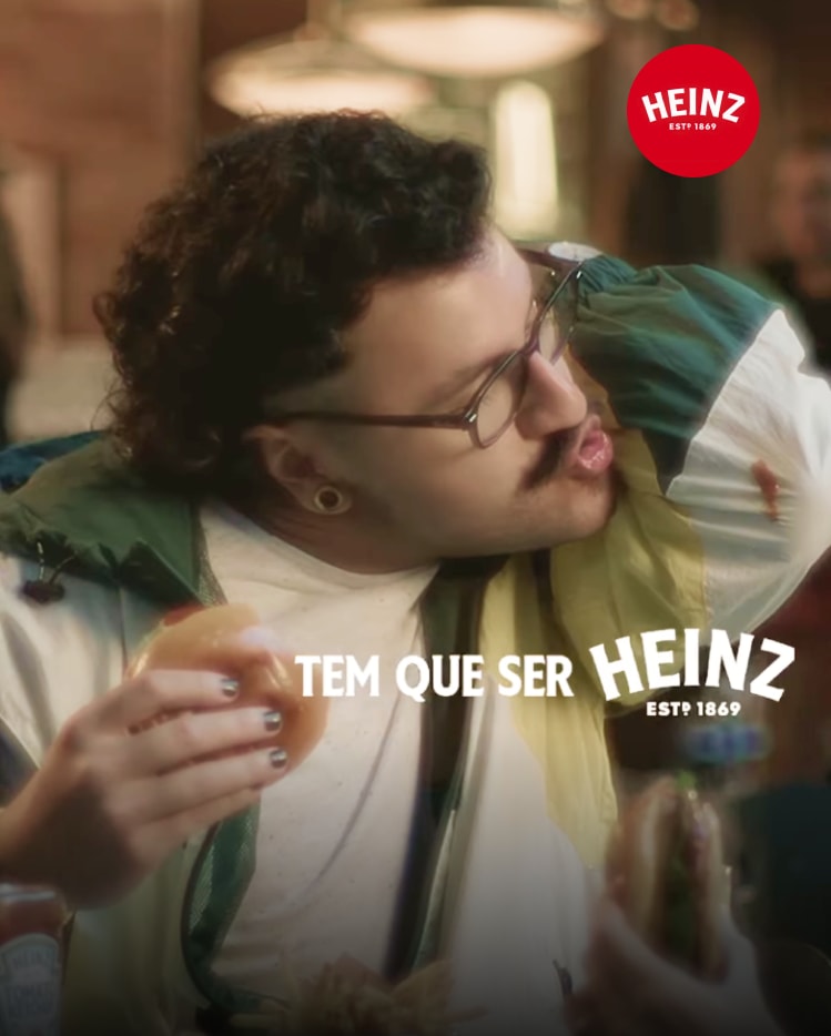 A man in a tracksuit licking a sauce stain off his sleeve while holding a burger.