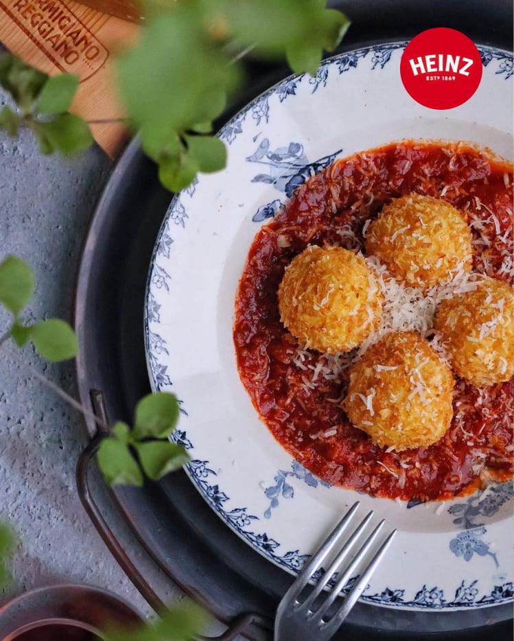 Three golden arancini rice balls served on a bed of red tomato sauce.