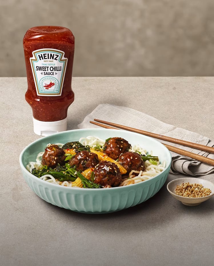 A bowl of noodles and greens topped with glazed meatballs, featuring Heinz Sweet Chilli Sauce.