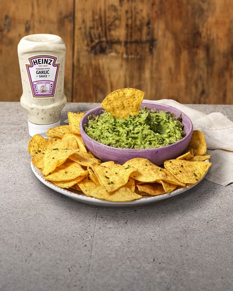 A bowl of vibrant green cabbage dip surrounded by crunchy tortilla chips, served with Heinz Garlic Sauce.