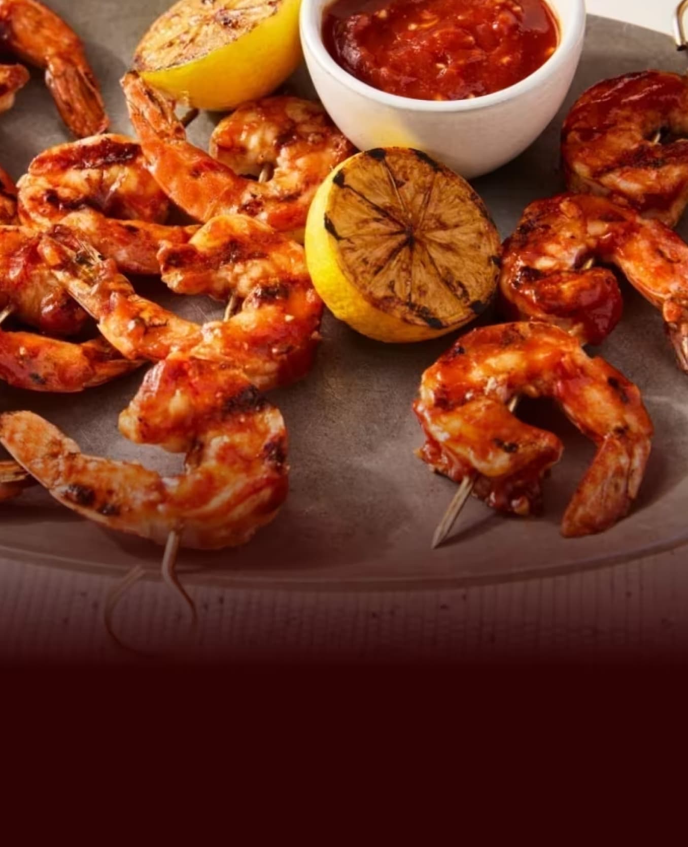 Grilled shrimp skewers served with a bowl of Heinz sauce and grilled lemon halves.