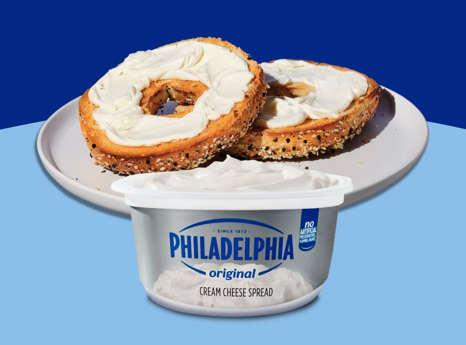 A bagel with cream cheese, over a blue background, with a Philadelphia tub