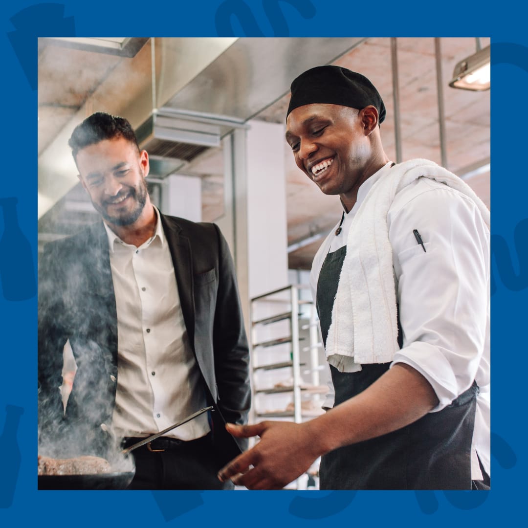 A chef and manager in a kitchen, reviewing food being cooked in a pan