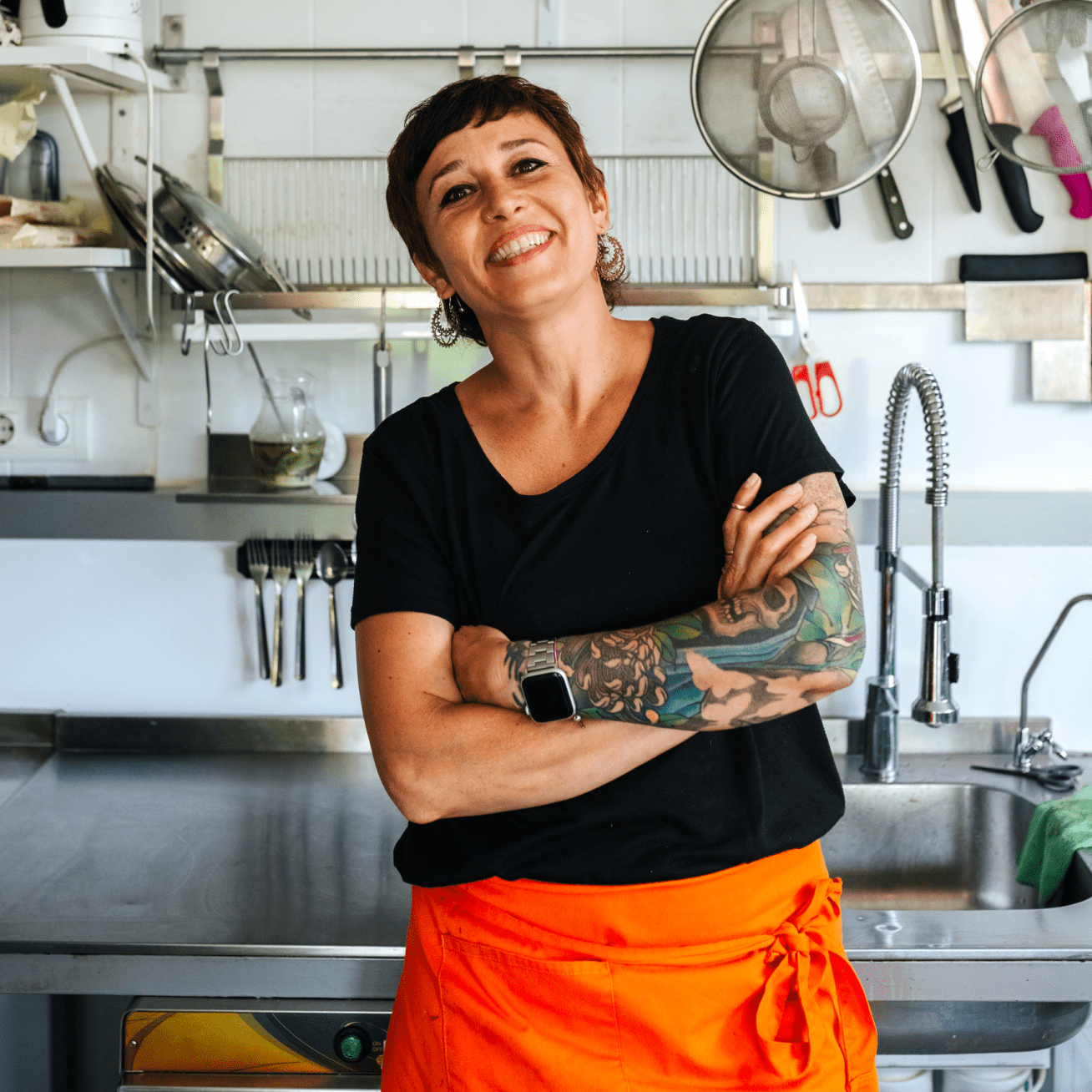 Une femme souriante et tatouée se tient dans une cuisine.