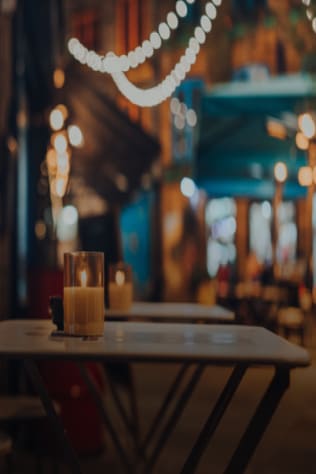 Empty outdoor restaurant tables with candles in the evening, blurred background of street lights and storefronts.