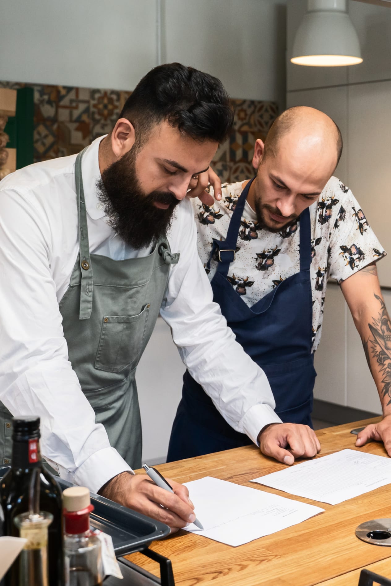 Two male chefs look down on menu laying on a wood countertop.