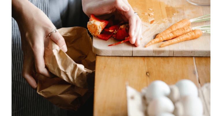 A woman empties vegetables from a paper bag onto a cutting board with carrots and peppers.
