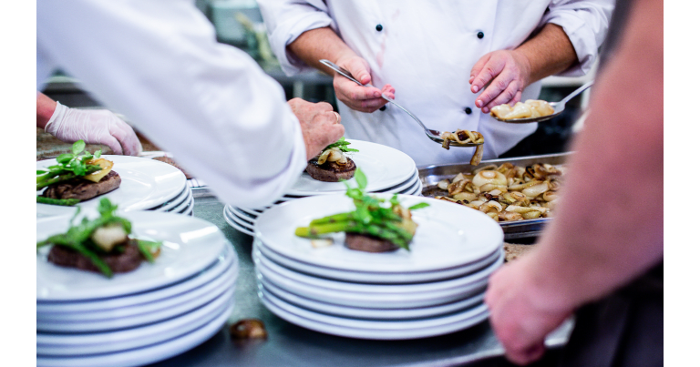Chefs plating meat dishes with vegetables in a professional kitchen.