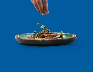 Hand placing herbs on a plate of food