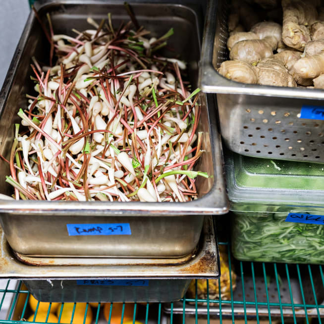 Prepared vegetables in a container sitting on a restaurant kitchen produce shelf