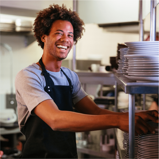 Smiling man in apron stands by a shelf of plates.