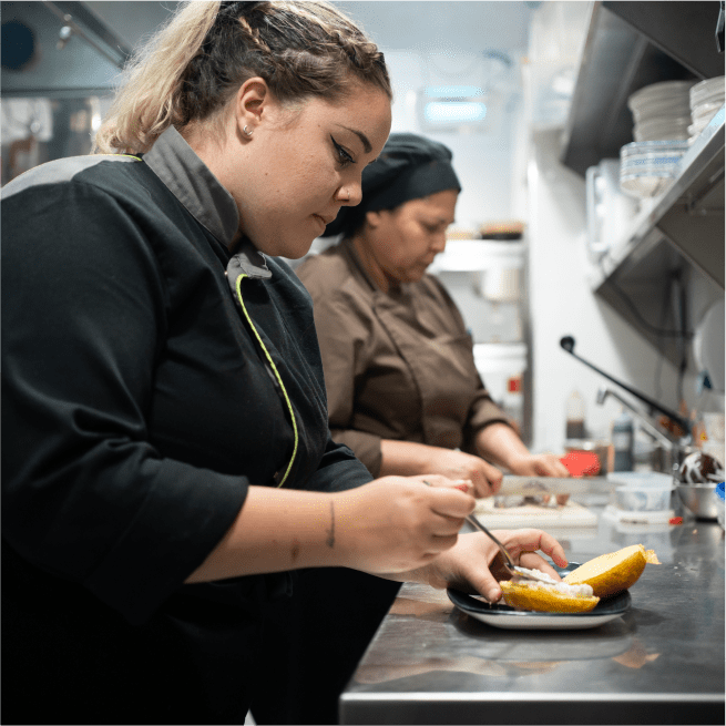 Une chef prépare un plat de mangue dans une cuisine.