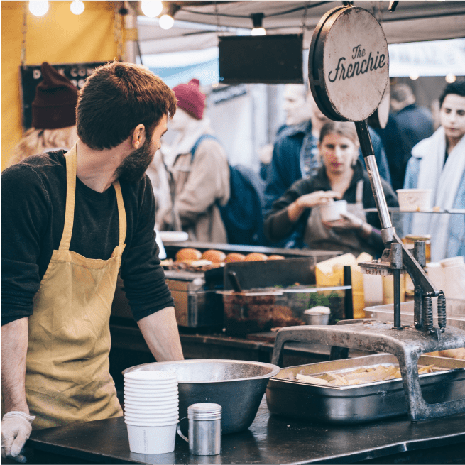 Bearded man at a food stall selling french fries.