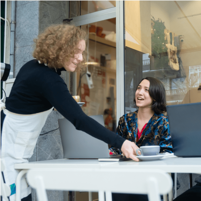 Waitress serves coffee to a smiling customer at an outdoor cafe.